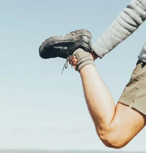 A man stretching his leg while wearing hiking boots and hiking socks.