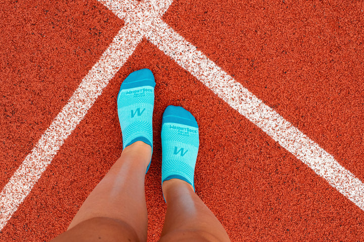 A person standing on a track in Wrightsock Turquoise Racer Tab socks.